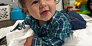 Kolton joined the competition — help win amazing prizes! baby, child, plaid_shirt, smiling, lying_down, blanket, indoor, toy, diapers, floor, happy, cute, face, clothing, person, toddler, blue, white, home, playful