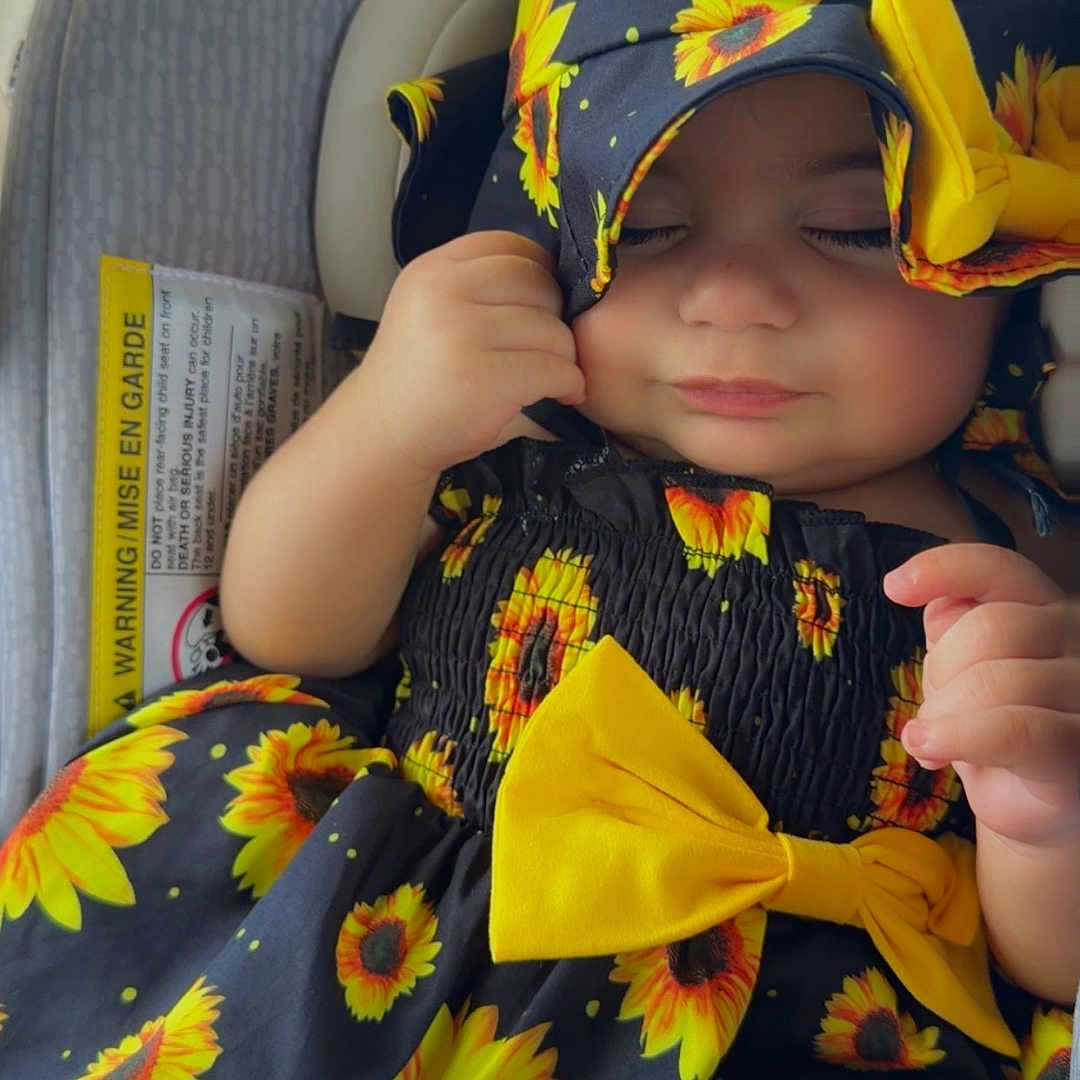Sally joined the competition — help win amazing prizes! baby, car_seat, child, closeup, clothing, comfort, cute, dress, face, hand, hat, headwear, indoors, infant, peaceful, portrait, resting, sleeping, sunflower_pattern, yellow_bow