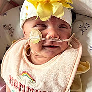 Calianna joined the competition — help win amazing prizes! baby, infant, headband, flower, bib, nasal_tube, medical_device, close_up, face, expression, lying_down, pillow, pattern, butterfly, yellow, pink, clothing, person, newborn, soft_light