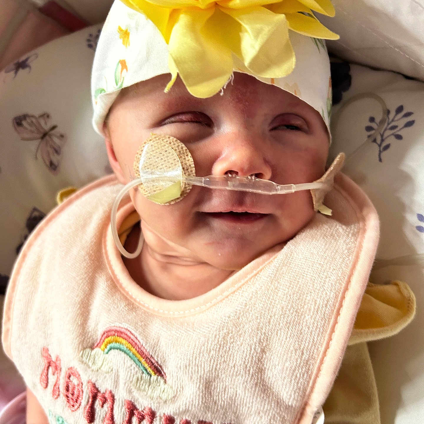 Calianna joined the competition — help win amazing prizes! baby, bib, butterfly, close_up, clothing, expression, face, flower, headband, infant, lying_down, medical_device, nasal_tube, newborn, pattern, person, pillow, pink, soft_light, yellow