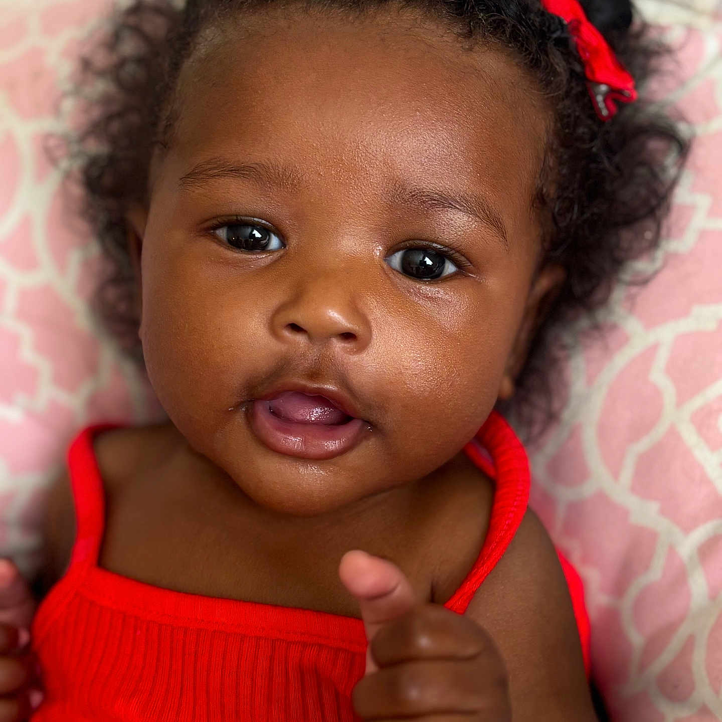 Areya joined the competition — help win amazing prizes! baby, child, close_up, curly_hair, cute, expression, face, happy, headshot, indoors, infant, person, pink_background, pointing_finger, portrait, red_bow, red_clothing, skin, smiling, young