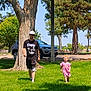 car, casual_clothing, child, daylight, dress, grass, greenery, hat, man, nature, outdoor, park, person, recreation, running, summer, sunlight, tree, tshirt, walking