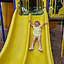 casual_clothing, child, curly_hair, daytime, fun, grass, happy, joy, nature, outdoor, play, playground, recreation, shoes, slide, smile, summer, toddler, trees, yellow_slide