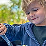 William participe au concours pour gagner de l'argent avec cette photo : blonde_hair, blue_jacket, bowl, boy, casual_clothing, child, close_up, cute, daylight, eating, food, happy, nature, outdoor, pasta, playful, portrait, smile, utensil, young_child