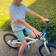 Liam a rejoint le concours — aidez-le/la à gagner de superbes lots ! child, boy, bicycle, bike, outdoor, grass, path, cap, shorts, tshirt, shoes, sunlight, shadow, greenery, playing, summer, casual_clothing, young, helmet_absent, exercise