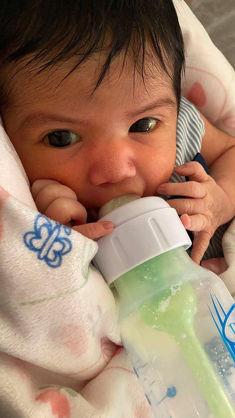 Alessandra is registered to the contest to win money with this photo: baby, baby_bottle, cheek, chin, drinkware, ear, eyebrow, eyelash, facial_expression, finger, gesture, hand, head, lip, liquid, mouth, nose, organ, person, product