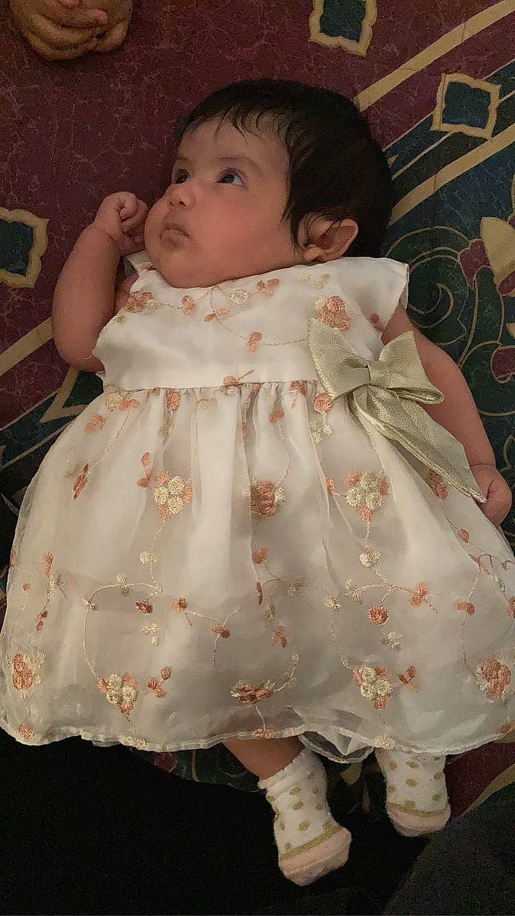 Alessandra is registered to the contest to win money with this photo: arm, baby, baby_toddler_clothing, cheek, day_dress, dress, embellishment, eye, face, head, headgear, human_body, iris, lip, neck, one_piece_garment, outerwear, person, pink, skin