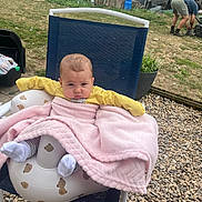 Isabella is registered to the contest to win money with this photo: baby, blanket, chair, outdoor, garden, person, grass, rock, plant, fence, seat, clothing, footwear, sock, head, face, expression, cushion, yard, casual