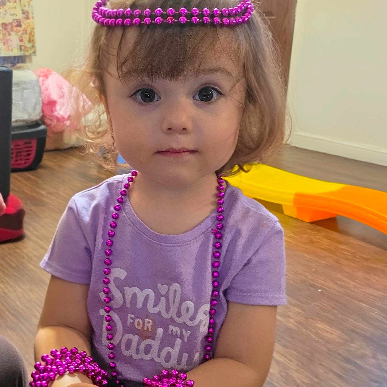 Jailyne joined the competition — help win amazing prizes! accessories, beads, bracelets, child, clothing, curly_hair, door, expression, eyes, face, floor, hands, indoor, necklaces, purple_shirt, sitting, toddler, toy, window, wooden_floor