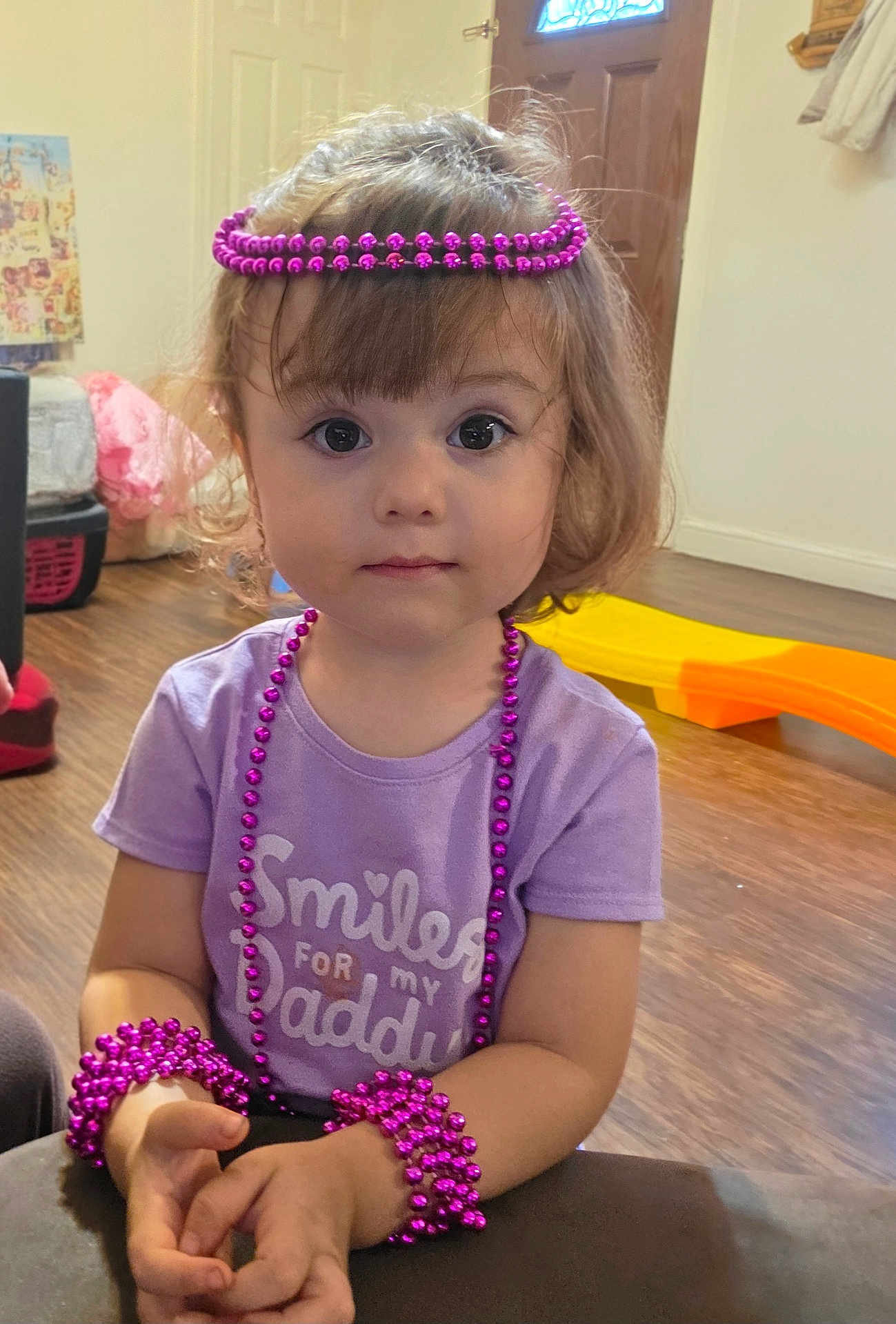 Jailyne joined the competition — help win amazing prizes! toddler, child, purple_shirt, beads, bracelets, necklaces, indoor, toy, floor, curly_hair, face, eyes, hands, sitting, wooden_floor, door, window, clothing, expression, accessories