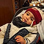 child, toddler, baby, beanie, winter_coat, scarf, car_seat, stroller, big_eyes, smile, hand, mittens, warm_clothing, indoor, cafe, wood_paneling, bokeh, portrait, cozy, seatbelt