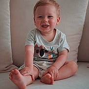 Lucas a rejoint le concours — aidez-le/la à gagner de superbes lots ! barefoot, blond_hair, child, clothing, comfort, couch, cushion, cute, face, happy, home, indoor, light_skin, portrait, shorts, sitting, smiling, toddler, tshirt, young_child