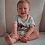barefoot, blond_hair, child, clothing, comfort, couch, cushion, cute, face, happy, home, indoor, light_skin, portrait, shorts, sitting, smiling, toddler, tshirt, young_child