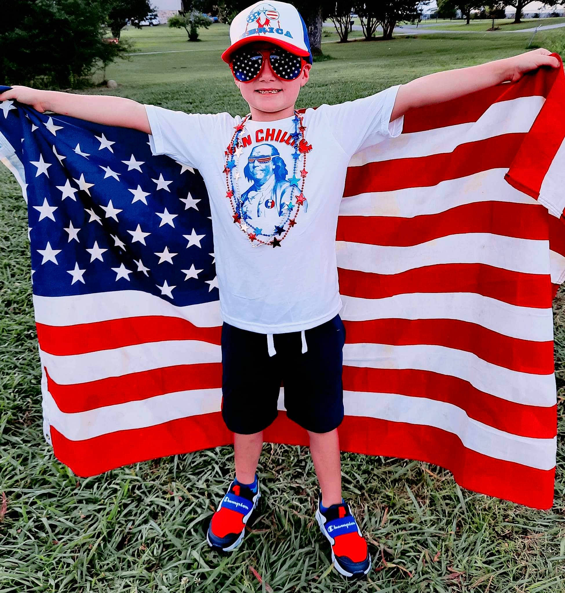 Chevy is registered to the contest to win money with this photo: cap, event, flag, flag_day_usa, flag_of_the_united_states, gesture, glasses, goggles, grass, hat, headgear, headwear, holiday, joy, person, shoe, shorts, sleeve, smile, sportswear