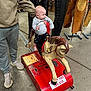 adult_hand, baby, baby_clothes, child, clothing, coin_operated_ride, concrete_floor, floor, grip, indoor, leather_chaps, person, ride, shoes, stall, store, toy, toy_horse, vintage, western_gear