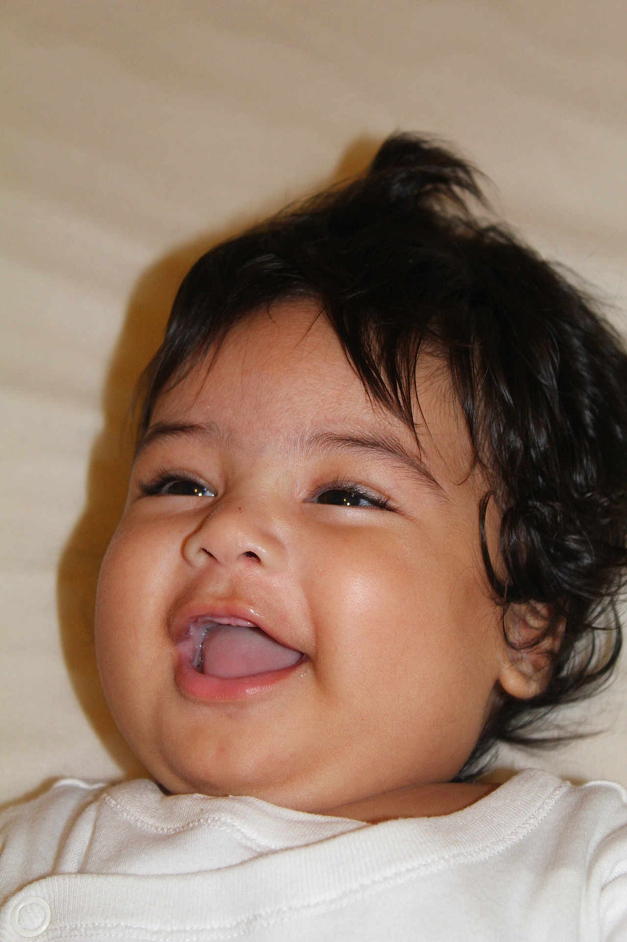 Matahi a rejoint le concours — aidez-le/la à gagner de superbes lots ! baby, infant, child, smiling, laughing, face, dark_hair, tongue, teeth, cheek, eyes, skin, portrait, close_up, white_shirt, lying_down, bed, happy, cute, drool