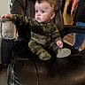 baby, child, infant, sitting, recliner, armchair, leather, camouflage, onesie, blue_eyes, curly_hair, wide_eyed, indoors, living_room, adult, furniture, portrait, seated, home, photography