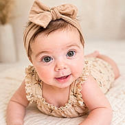 Luiza is registered to the contest to win money with this photo: baby, infant, child, headband, bow, cute, smile, lying_down, quilt, soft_texture, indoors, portrait, closeup, skin, eyes, hand, clothing, neutral_background, adorable, happy