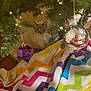 cat, christmas_tree, ornament, purple_ornament, silver_ornament, blanket, zigzag_pattern, indoor, holiday, festive, pet, animal, fur, relaxed, decorations, lights, greenery, cozy, home, cute