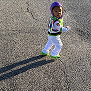 Marion joined the competition — help win amazing prizes! child, costume, buzz_lightyear, outdoor, asphalt, shadow, sunlight, walking, purple_hood, green_shoes, white_pants, toy_story, young, person, face, curious, standing, daylight, casual, playful