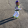 child, costume, buzz_lightyear, outdoor, asphalt, shadow, sunlight, walking, purple_hood, green_shoes, white_pants, toy_story, young, person, face, curious, standing, daylight, casual, playful