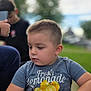 child, toddler, boy, water_bottle, shirt, lemonade_print, outdoor, park, greenery, trees, person, blurred_background, short_hair, casual_clothing, daylight, holding, concentration, portrait, candid, summer