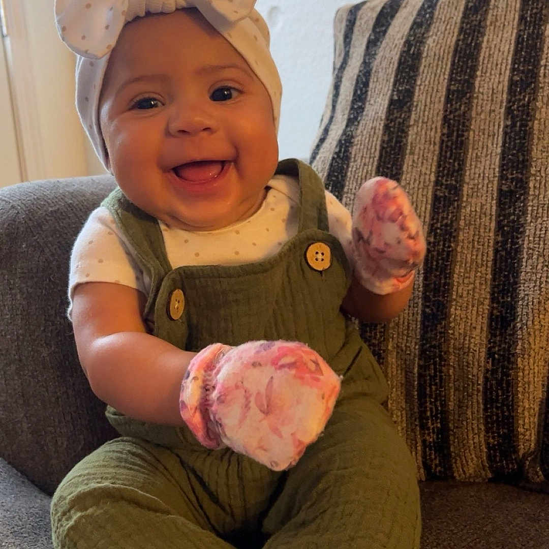 Xayoni joined the competition — help win amazing prizes! baby, smiling, child, infant, couch, overalls, mittens, headband, bow, happy, indoors, striped_pillow, socks, seated, cute, portrait, cozy, furniture, living_room, person