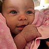 baby, infant, child, smiling, portrait, close_up, pink_blanket, cozy, indoor, face, eyes, blue_eyes, hand, cuddling, soft_fabric, warm_lighting, happy, sitting, home, candid