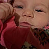 baby, infant, child, face, portrait, sleepy, lying_down, close_up, eyes, cheeks, adult_hand, pink_blanket, patterned_clothing, colorful, indoor, bedding, soft_lighting, home, candid, cute