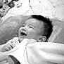 baby, blanket, smile, cushion, toy, water_bottle, infant, happy, indoors, child, soft_texture, face, lying_down, monochrome, cozy, cute, hair, clothing, hand, portrait