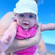 Evie is registered to the contest to win money with this photo: adult, arm, baby, beach, blue_sky, child, closeup, hand, happy, hat, infant, outdoor, person, pink_clothing, portrait, sky, smiling, summer, sun_hat, vacation