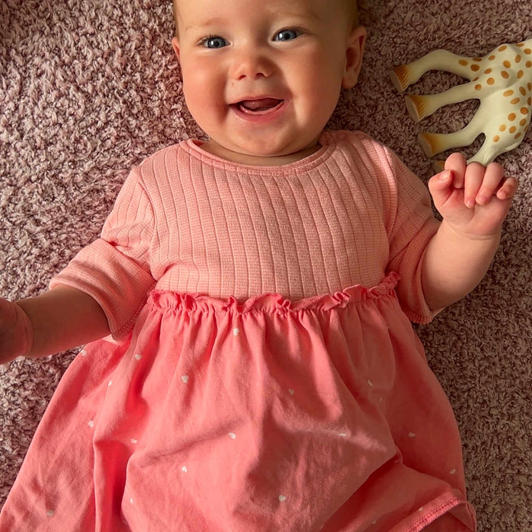 Isabella joined the competition — help win amazing prizes! baby, baby_girl, child, cozy, cute, giraffe_toy, happy, indoor, infant, lying_down, person, pink_dress, playful, rug, small_child, smiling, soft, stuffed_animal, texture, toy