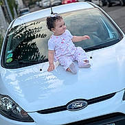 Layane participe au concours pour gagner de l'argent avec cette photo : toddler, child, car, ford, white_car, curly_hair, outdoor, street, license_plate, sitting, clothing, daytime, vehicle, sidewalk, urban, portrait, cute, baby, head, expression