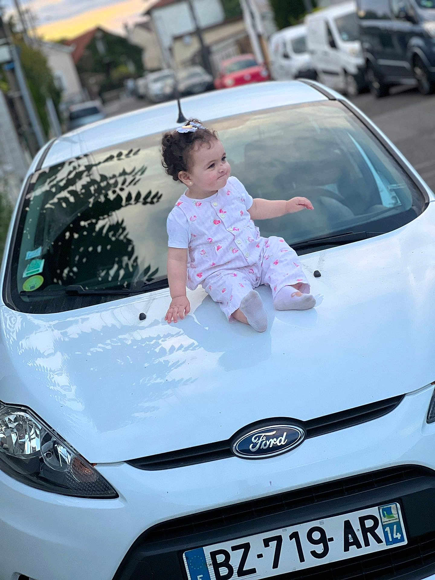Layane participe au concours pour gagner de l'argent avec cette photo : toddler, child, car, ford, white_car, curly_hair, outdoor, street, license_plate, sitting, clothing, daytime, vehicle, sidewalk, urban, portrait, cute, baby, head, expression