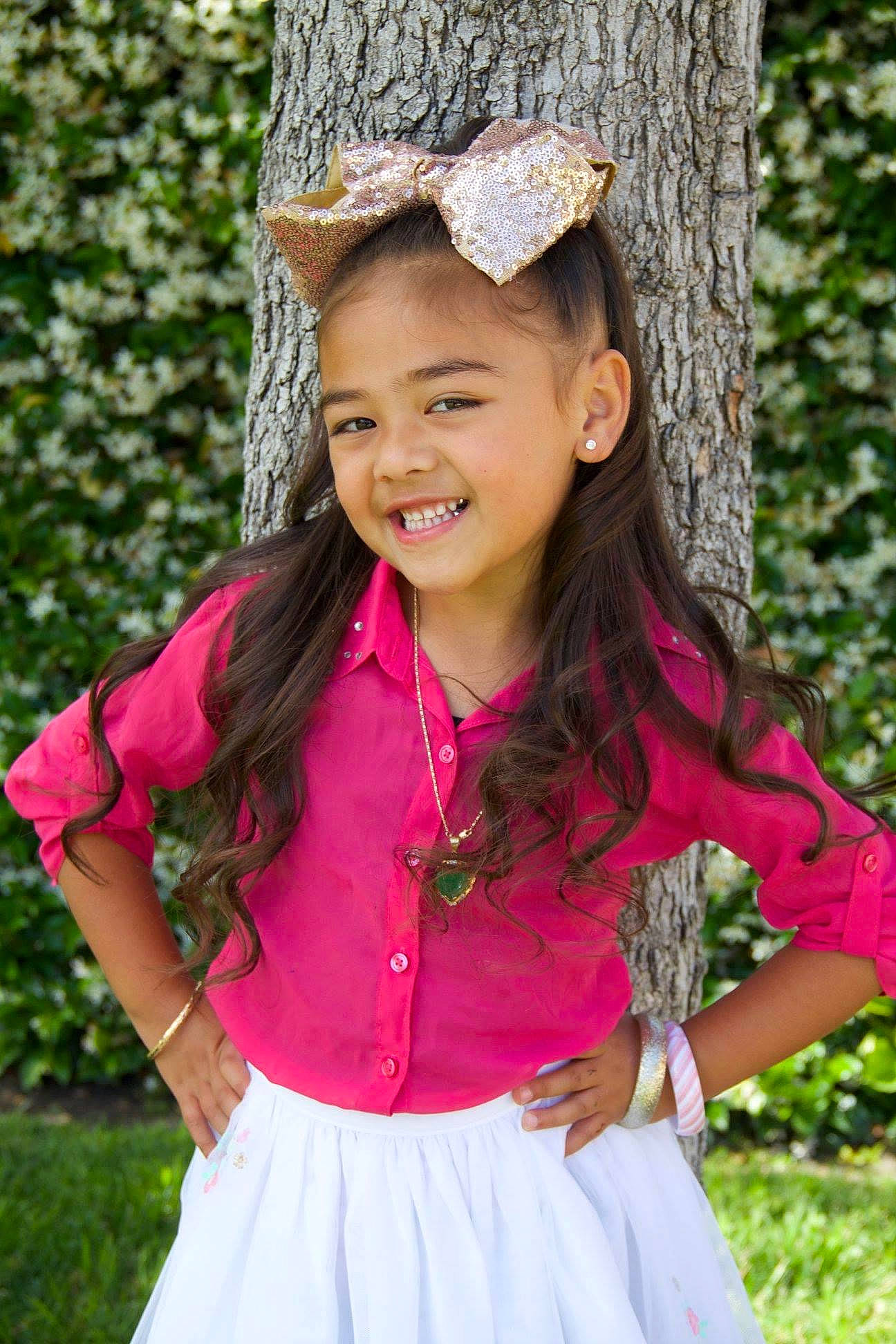 Isabella is registered to the contest to win money with this photo: beauty, cap, eye, grass, happy, head, headgear, joy, long_hair, people_in_nature, person, photograph, pink, plant, shoulder, sleeve, smile, toddler, tree, trunk