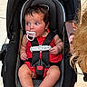 baby, infant, car_seat, pacifier, red_dress, child, straps, safety_harness, curly_hair, phone, video_call, indoors, tile_floor, person, cute, wide_eyes, seated, expression, secure, modern