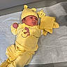 Ma Lani joined the competition — help win amazing prizes! baby, infant, yellow_clothing, hat, plush_toy, blanket, lying_down, cute, newborn, indoors, soft_toys, smiling_face_design, headwear, sleepwear, child, person, fabric, footwear, resting, cozy