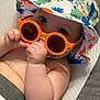 baby, infant, sunglasses, hat, dinosaur_print, orange, cute, child, seat, cushion, blanket, skin, hand, face, eyes, indoor, relaxing, summer, accessory, comfort