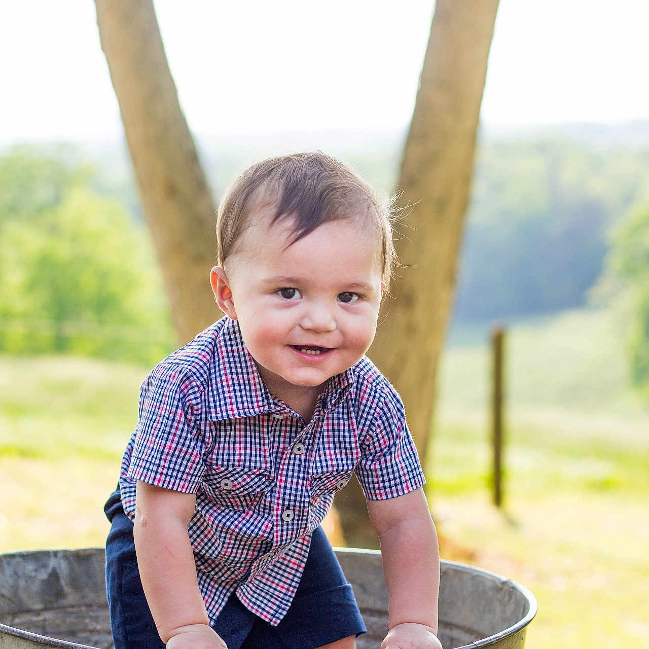 Nolan is registered to the contest to win money with this photo: baby, child, countryside, cute, daylight, grass, happy, metal_tub, nature, outdoor, person, plaid_shirt, playful, portrait, shorts, smiling, summer, sunlight, toddler, tree