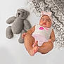 baby, infant, headband, pink, knitted_toy, teddy_bear, blanket, patterned_blanket, white_background, clothing, cute, chubby, lying_down, indoors, soft_toy, baby_girl, portrait, child, relaxed, sleepy