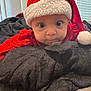 baby, child, santa_hat, red_clothing, blanket, bedroom, indoor, curious, face, wide_eyes, soft_texture, pillow, holiday, christmas, infant, person, cute, portrait, cozy, resting