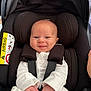 baby, car_seat, smiling, infant, white_clothing, blanket, safety_harness, airbag_warning, indoors, child, cute, person, seatbelt, happy, small_hands, head_support, newborn, comfort, closeup, portrait