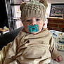 baby, child, pacifier, hat, knitted_hat, beige_clothing, indoor, portrait, cute, infant, face, sitting, cozy, warm_clothing, headwear, young_child, person, furniture, blanket, comfort