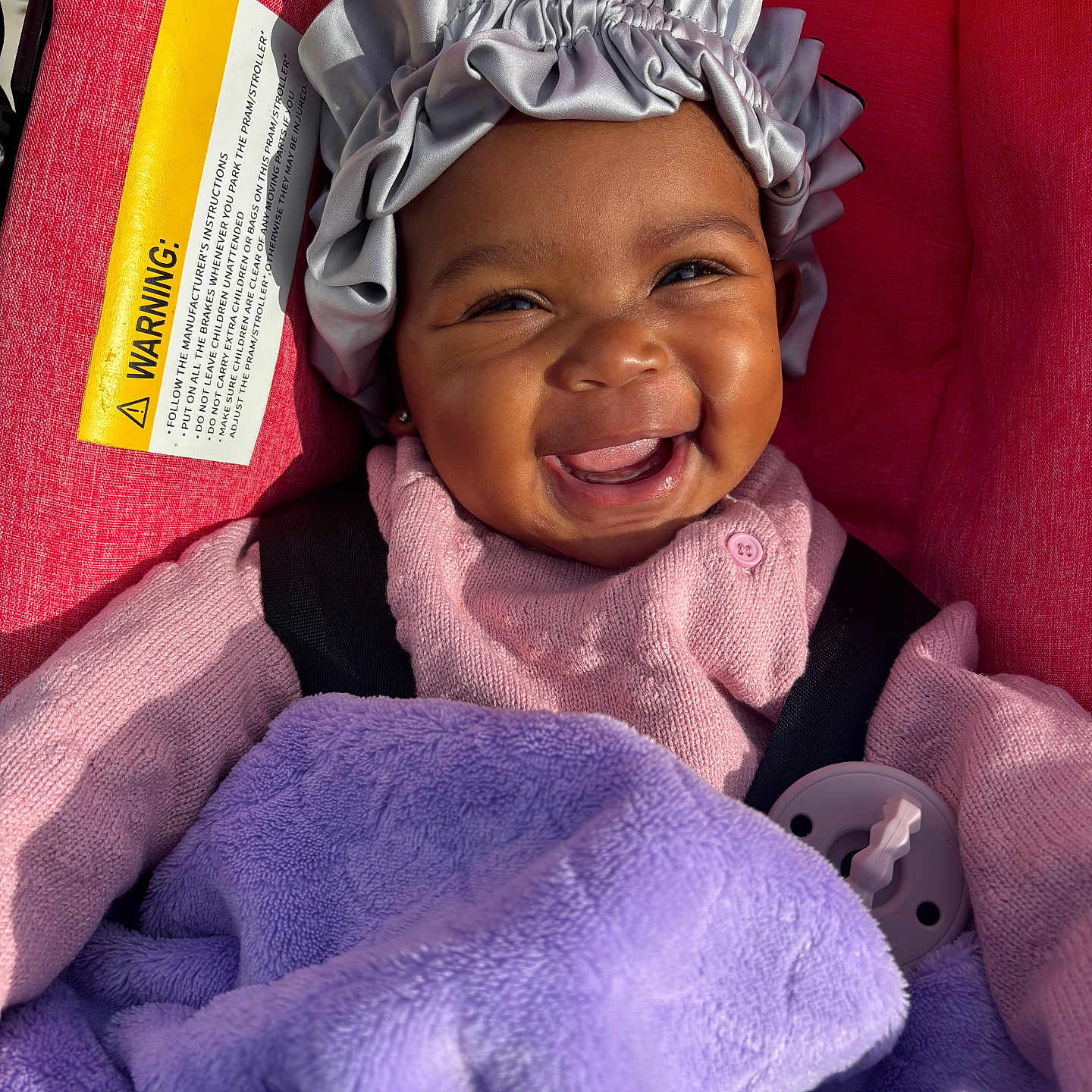 Naveah joined the competition — help win amazing prizes! baby, smiling, blanket, purple_blanket, red_cushion, silver_bonnet, pink_clothing, happy, infant, face, closeup, indoor, cute, child, person, portrait, cozy, warm, seat, sunlight