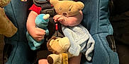 John is registered to the contest to win money with this photo: baby, car_seat, plush_toy, teddy_bear, blue, red_hat, striped_socks, infant, child, soft_toy, blanket, cute, smiling, indoor, seat_belt, clothing, headwear, person, comfort, resting