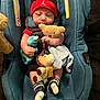 baby, car_seat, plush_toy, teddy_bear, blue, red_hat, striped_socks, infant, child, soft_toy, blanket, cute, smiling, indoor, seat_belt, clothing, headwear, person, comfort, resting