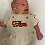 baby, infant, smiling, overalls, striped_clothing, red_car_patch, lying_down, white_background, happy, cute, child, person, clothing, button, shorts, hand, head, face, eyes, mouth