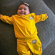 Laura is registered to the contest to win money with this photo: baby, child, yellow_clothing, socks, headband, smiling, lying_down, couch, gray_texture, cute, infant, toddler, bear_patch, comfortable, indoors, portrait, happy, cozy, soft_surface, person