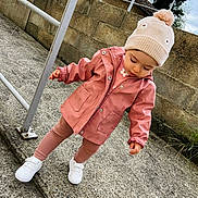 Lyana a rejoint le concours — aidez-le/la à gagner de superbes lots ! casual, child, cold_weather, concrete, curious, fashion, hat, leggings, metal_railing, outdoor, pink_raincoat, playful, pom_pom, standing, stone_wall, toddler, urban, white_shoes, winter_clothing, young_child