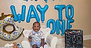 Ja'Majesty joined the competition — help win amazing prizes! baby, balloons, birthday, blue, cake, celebration, chair, child, decorations, floor, gold, happy, indoor, milestone_board, party, person, smiling, teddy_bear, white, white_rug